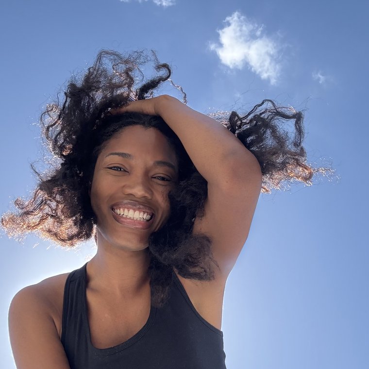 Ruqayyah laughing, hair caught by the wind against a blue sky