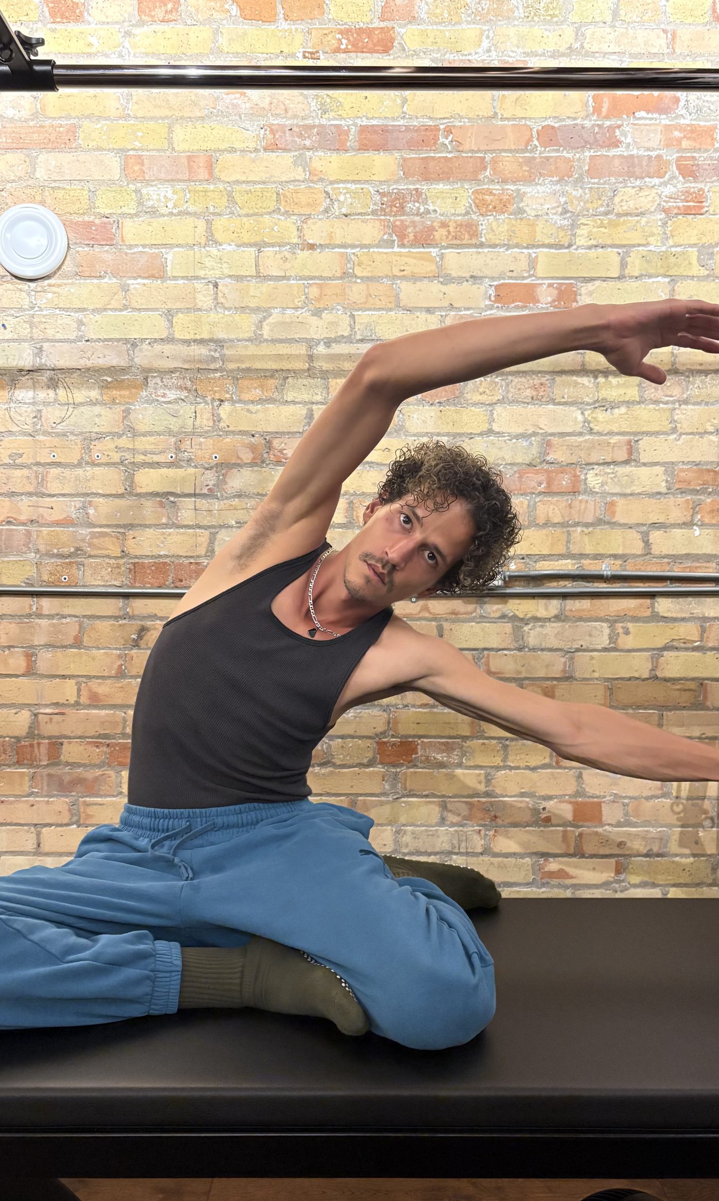 A client seated on the Cadillac table in a mermaid side stretch against a brick wall